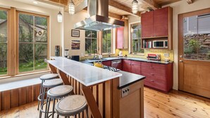 A kitchen with a central island, bar stools, wooden beams, and a view of the outdoors.
