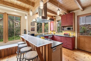 A kitchen with a central island, bar stools, wooden beams, and a view of the outdoors.