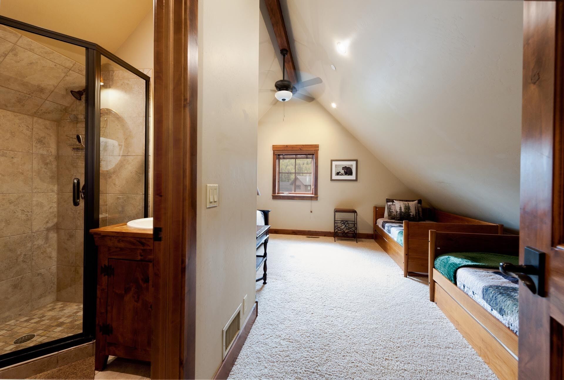 A bedroom with a sloped ceiling, a wooden bed, a bedside table, a window, and a ceiling fan.