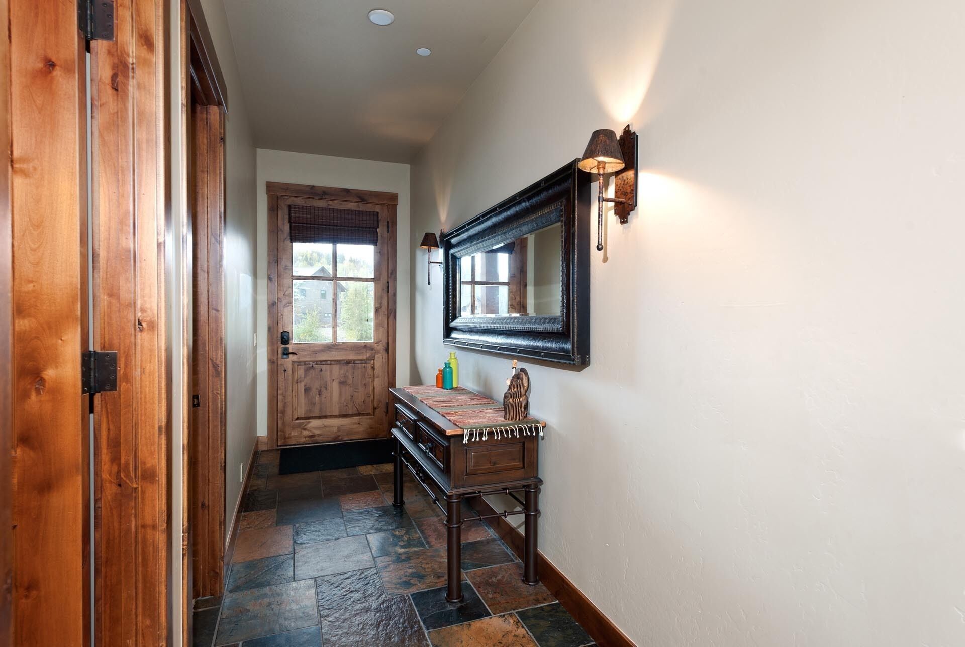 Un couloir avec une porte en bois, un banc et un miroir fixé au mur.