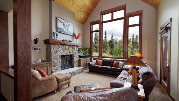 A cozy living room with a stone fireplace, leather sofas, and large windows offering a view of trees. - Home Across from Purg - Views, Deck/Fire Pit/Ping Pong/Shuffleboard (Durango)