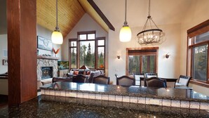 A spacious kitchen with granite countertops, a stone fireplace, and large windows offering a view of the forest. - Home Across from Purg - Views, Deck/Fire Pit/Ping Pong/Shuffleboard (Durango)