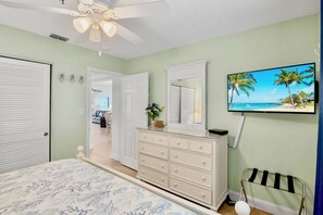 Un dormitorio con cama, cómoda, ventilador de techo y televisor en la pared.