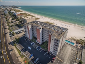 A multi-story hotel with a parking lot, a beach view, and a pool area.