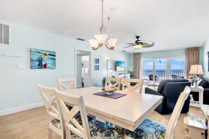 A modern living room with a dining area, a ceiling fan, and a view of the ocean.