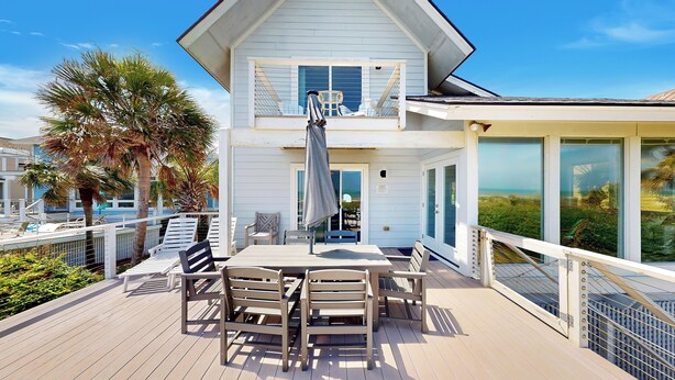 Une maison à deux étages avec un balcon, une table entourée de chaises et une vue sur l’océan.