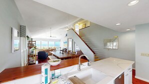 Une cuisine spacieuse avec un grand îlot central, un coin repas offrant une vue agréable et un escalier menant à un balcon.