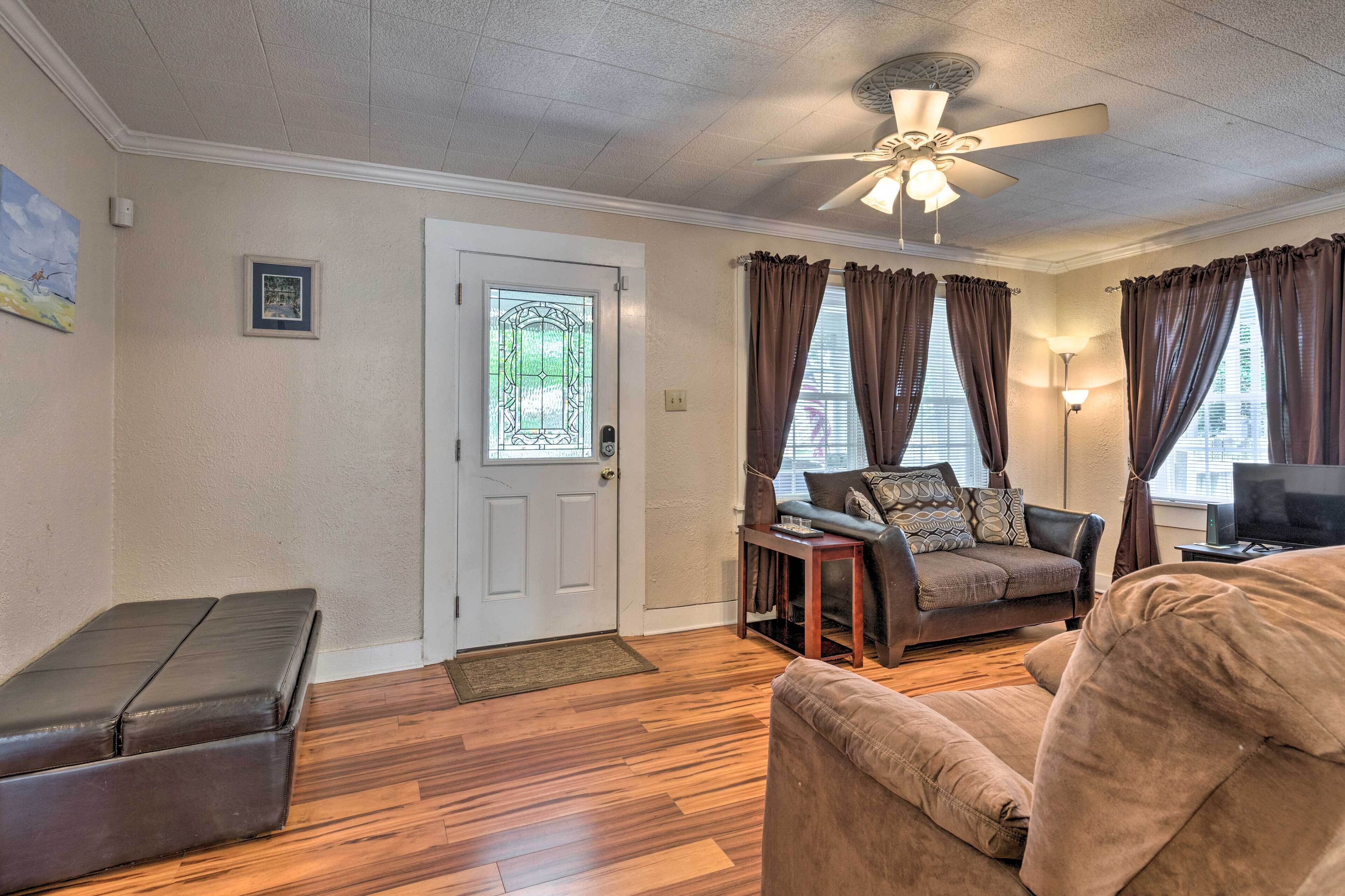 A living room with a ceiling fan, a door with a glass panel, a brown leather bench, a brown sofa, and a television.