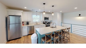 A modern kitchen with white cabinetry, stainless steel appliances, and a central island with bar stools. - 4 bedrooms, walk to the beach, large screened in porches! (Isle of Palms)