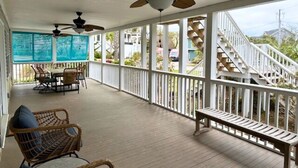 A covered porch with ceiling fans, wicker chairs, a wooden bench, and a staircase leading to an upper level. - 4 bedrooms, walk to the beach, large screened in porches! (Isle of Palms)