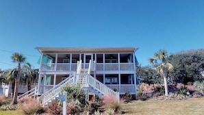 A two-story building with a balcony on the upper floor, surrounded by palm trees and shrubs. - 4 bedrooms, walk to the beach, large screened in porches! (Isle of Palms)
