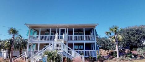A two-story building with a balcony on the upper floor, surrounded by palm trees and shrubs.