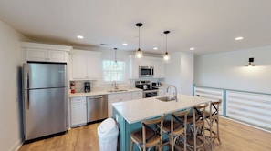 A modern kitchen with white cabinetry, stainless steel appliances, and a central island with bar stools.