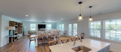 A spacious kitchen with a large island, wooden flooring, and a view of the outdoors through large windows.