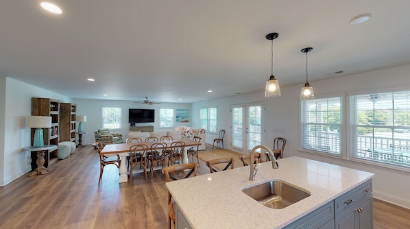 A spacious kitchen with a large island, wooden flooring, and a view of the outdoors through large windows.
