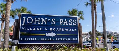 Une enseigne indiquant l’entrée de John’s Pass Village & Boardwalk, mettant en valeur les boutiques, les restaurants et les activités de divertissement.