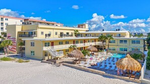 A hotel with multiple floors, a pool area with lounge chairs and umbrellas, and a sandy beach in front.