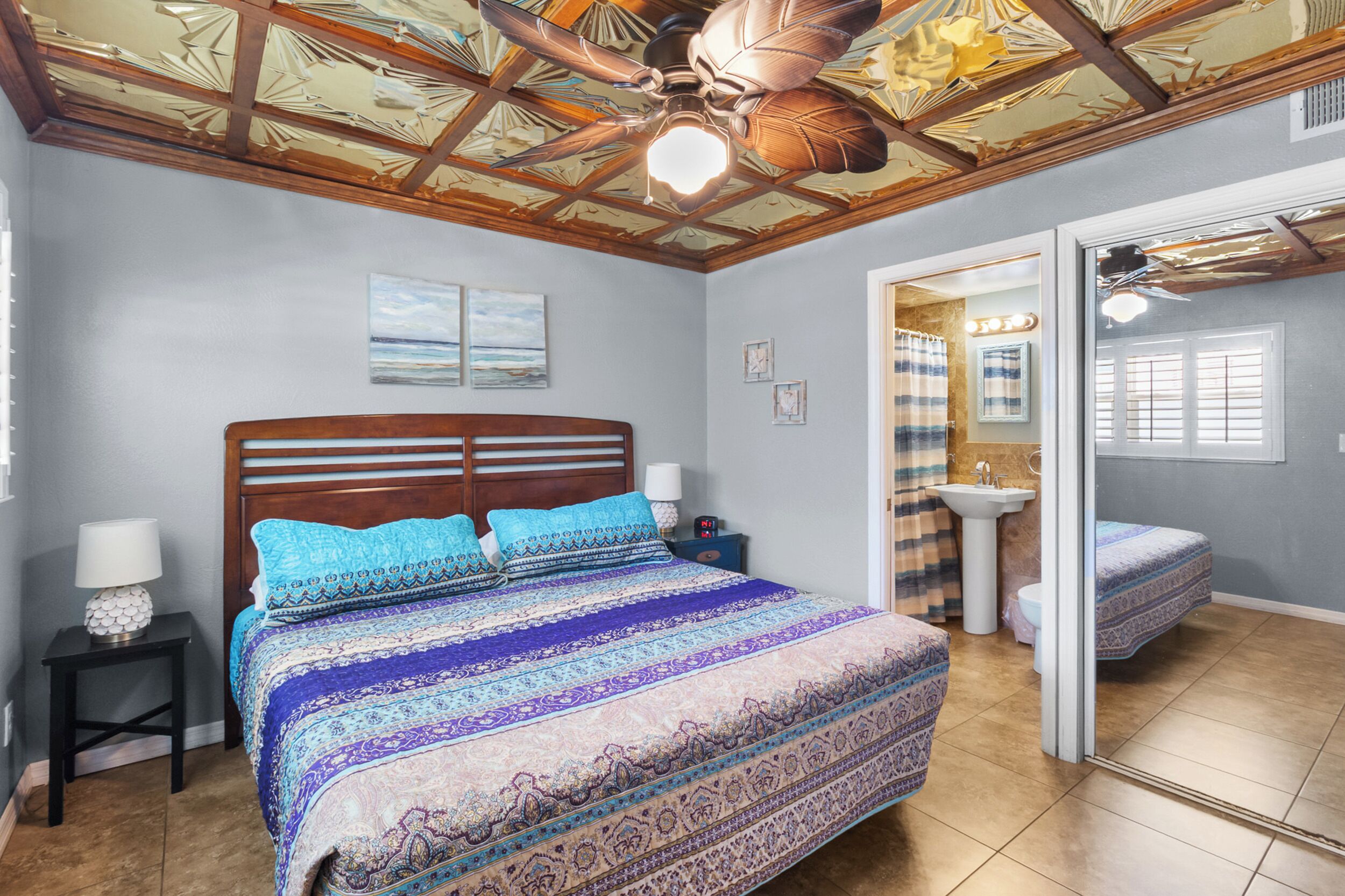 Ein Schlafzimmer mit einem großen Bett, einem Deckenventilator und einem Badezimmer mit Waschbecken und Spiegel.