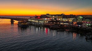 A waterfront hotel with a pier extending into the water, featuring multiple dining establishments and a view of the sunset.