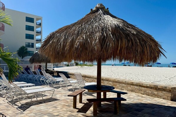 Un área de descanso frente a la playa con sombrillas de paja, sillas de lounge y una mesa.