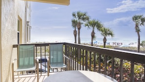 A balcony with a view of the beach, palm trees, and a clear sky.
