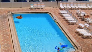 Ein rechteckiger Swimmingpool mit einer gefliesten Poolterrasse. Liegestühle und ein Whirlpoolbereich liegen an das Becken angrenzend.