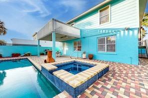 Piscina com deck revestido, varanda coberta e casa com fachada azul.