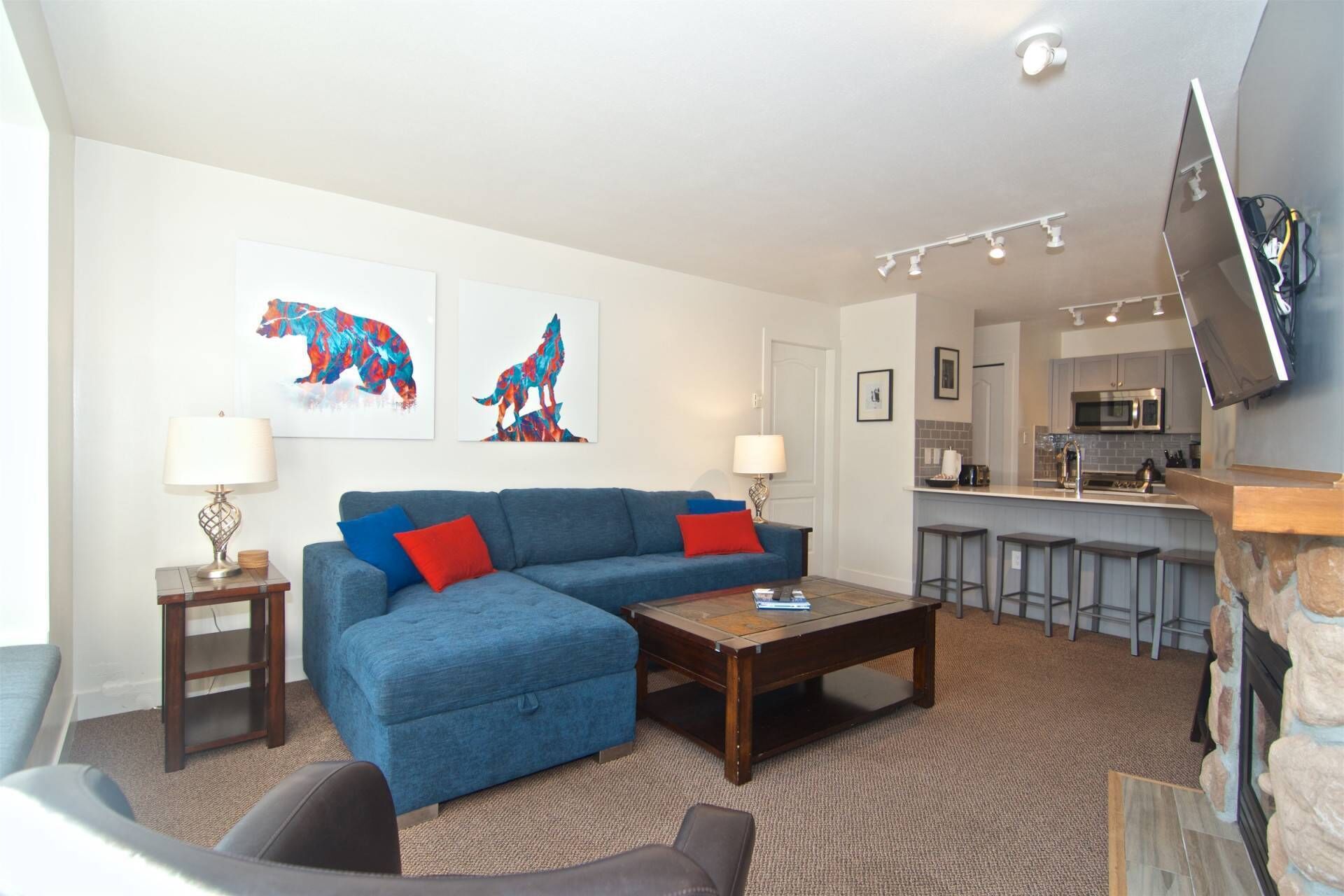 A living room with a blue sofa, a coffee table, and a TV mounted on the wall.