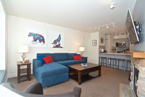 A living room with a blue sofa, a coffee table, and a TV mounted on the wall.