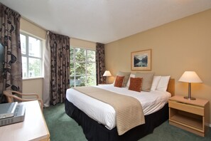 Ein Hotelzimmer mit einem Bett, zwei Nachttischen, einem Sessel, einem Schreibtisch mit Drucker und einem Fenster mit Vorhängen.