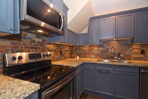 A kitchen with a brick backsplash, granite countertops, stainless steel appliances, and gray cabinetry. - Newly renovated Family Condo at Base of Blackcomb! New Central AC installed June 2026 (Whistler)