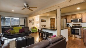 A modern living room with a leather sofa, a dining area with a bar stool, and a kitchen with wooden cabinets and stainless steel appliances. - Completely Remodeled Ski in/Ski Out condo - Amazing Views and Great Deck (Durango)