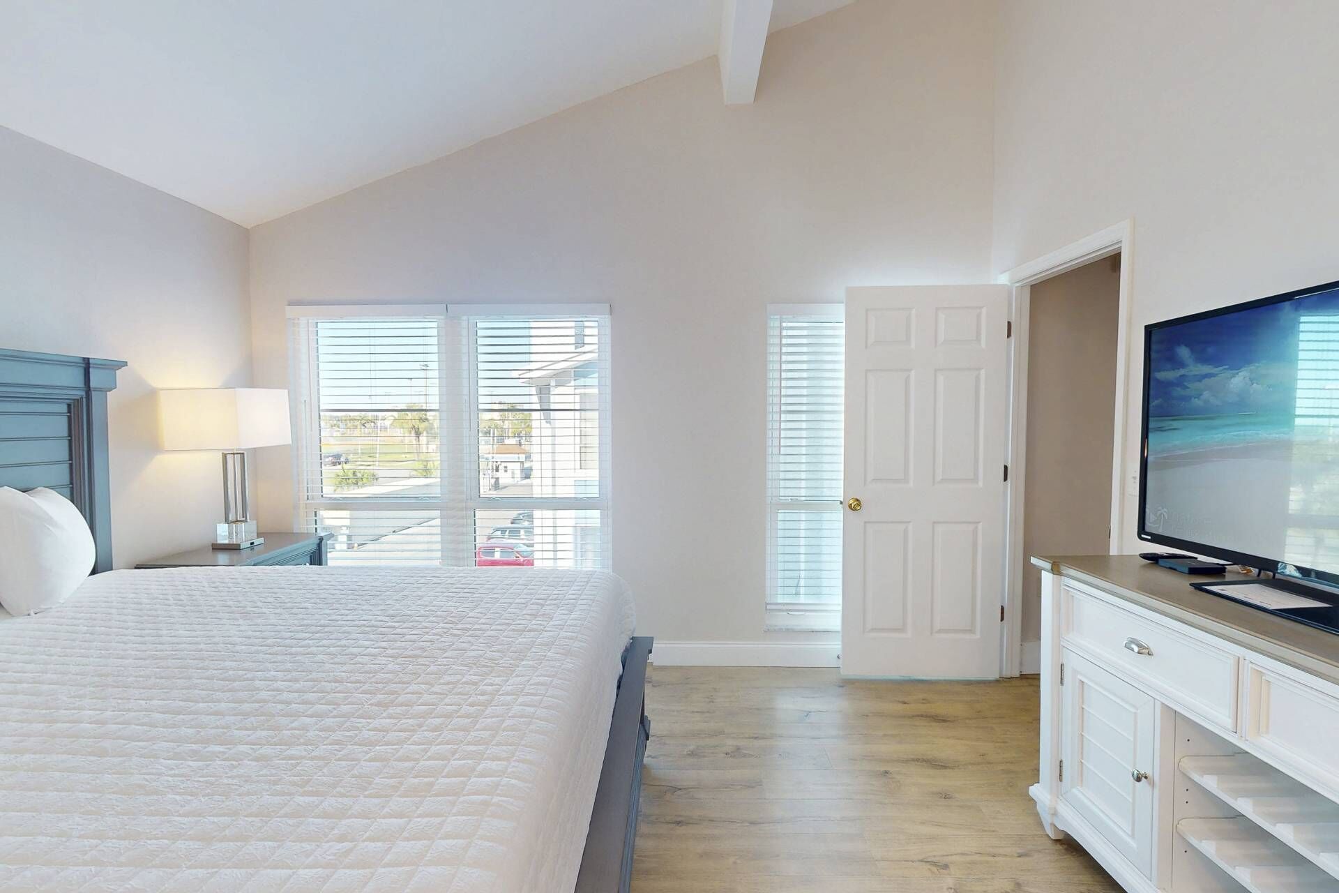 A bedroom with a bed, a TV, and a desk with a lamp.
