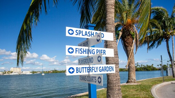 A signpost with directions to Splash Park, Fishing Pier, Playground, Butterfly Garden, and Tennis Courts. - 2-Level Madeira Beach Condo, Pool, Marina, Walk to Beach, Shops,  Dining +Tickets to Top Activities! (Madeira Beach)