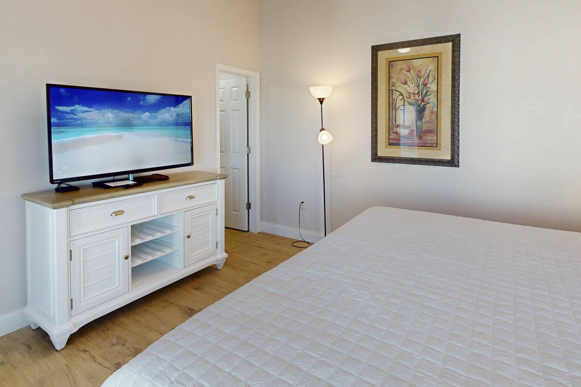 Een slaapkamer met een bed, een tv op een dressoir, een schilderij aan de muur en een vloerlamp.