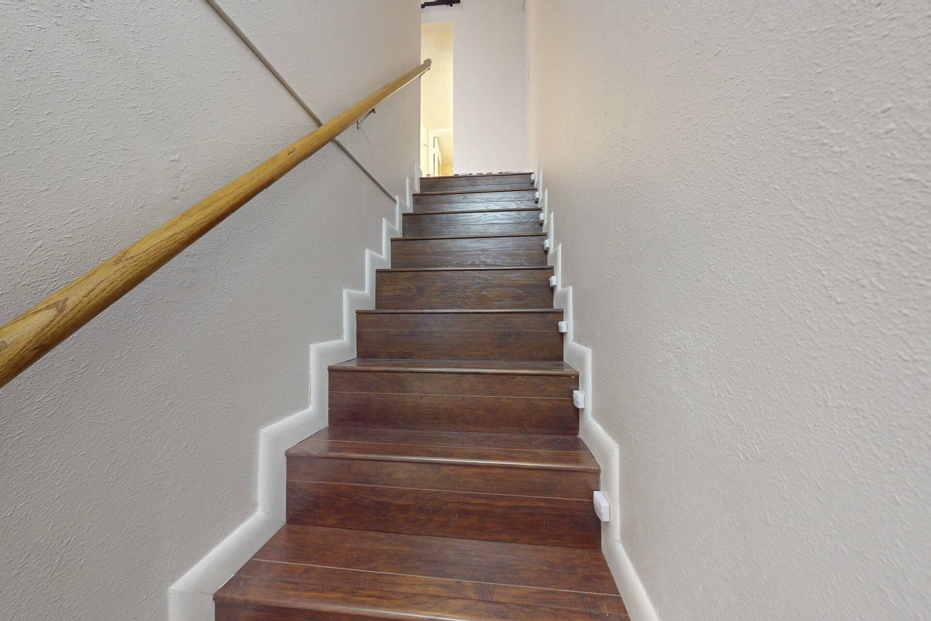 A wooden staircase with white trim against a plain wall.