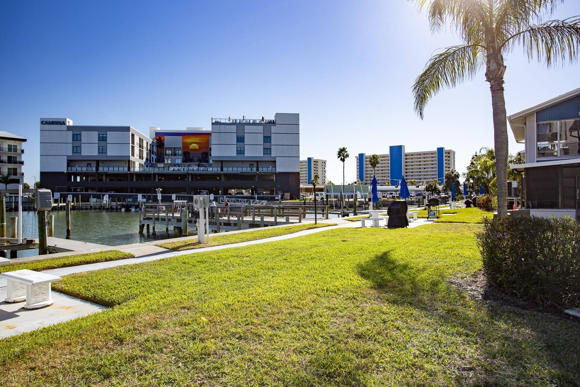 Un hotel frente al agua con un puerto deportivo, zonas verdes y edificios modernos al fondo.