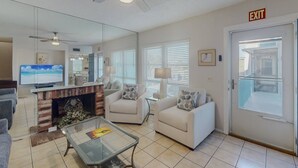 A living room with a fireplace, a television, and a glass coffee table. - 2-Level Madeira Beach Condo, Pool, Marina, Walk to Beach, Shops,  Dining +Tickets to Top Activities! (Madeira Beach)