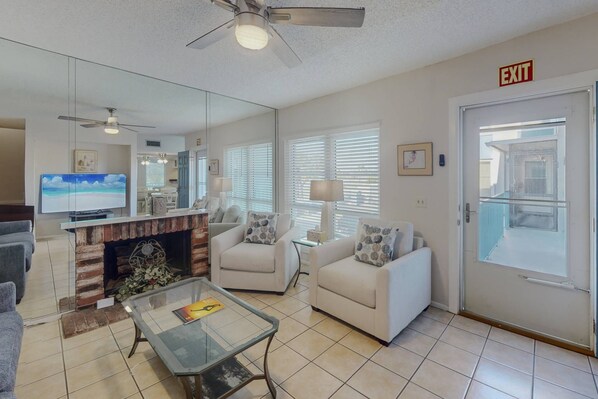 A living room with a fireplace, a television, and a glass coffee table. - 2-Level Madeira Beach Condo, Pool, Marina, Walk to Beach, Shops,  Dining +Tickets to Top Activities! (Madeira Beach)