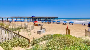 A beach with a wooden pier, beach umbrellas, and lounge chairs. - Beachfront, Pet-Friendly South Padre Island Condo (South Padre Island)