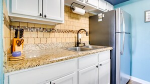 A kitchen with white cabinets, a granite countertop, a stainless steel refrigerator, and a tiled backsplash. - Beachfront, Pet-Friendly South Padre Island Condo (South Padre Island)
