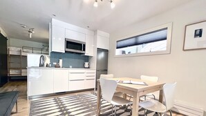 A modern kitchen with white cabinets, a microwave, and a refrigerator. There is a dining table with chairs and a patterned rug. - Chic, Modern | Walk Anywhere @ Viking Lodge 206 (Telluride)