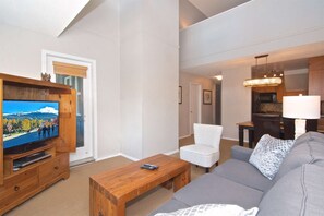 A living room with a TV, wooden coffee table, grey sofa, and white patterned chair.