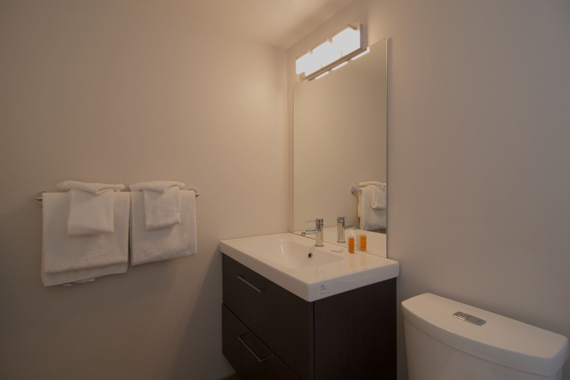 A bathroom with a white sink, dark cabinet, and a white toilet. There are two white towels hanging on the wall.