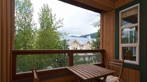 A wooden balcony with a table and chairs, overlooking a house with a blue roof and trees. - Renovated, Village location. Walk to lifts ,amenities, modern décor, hot tub closed for renovation. (Whistler)
