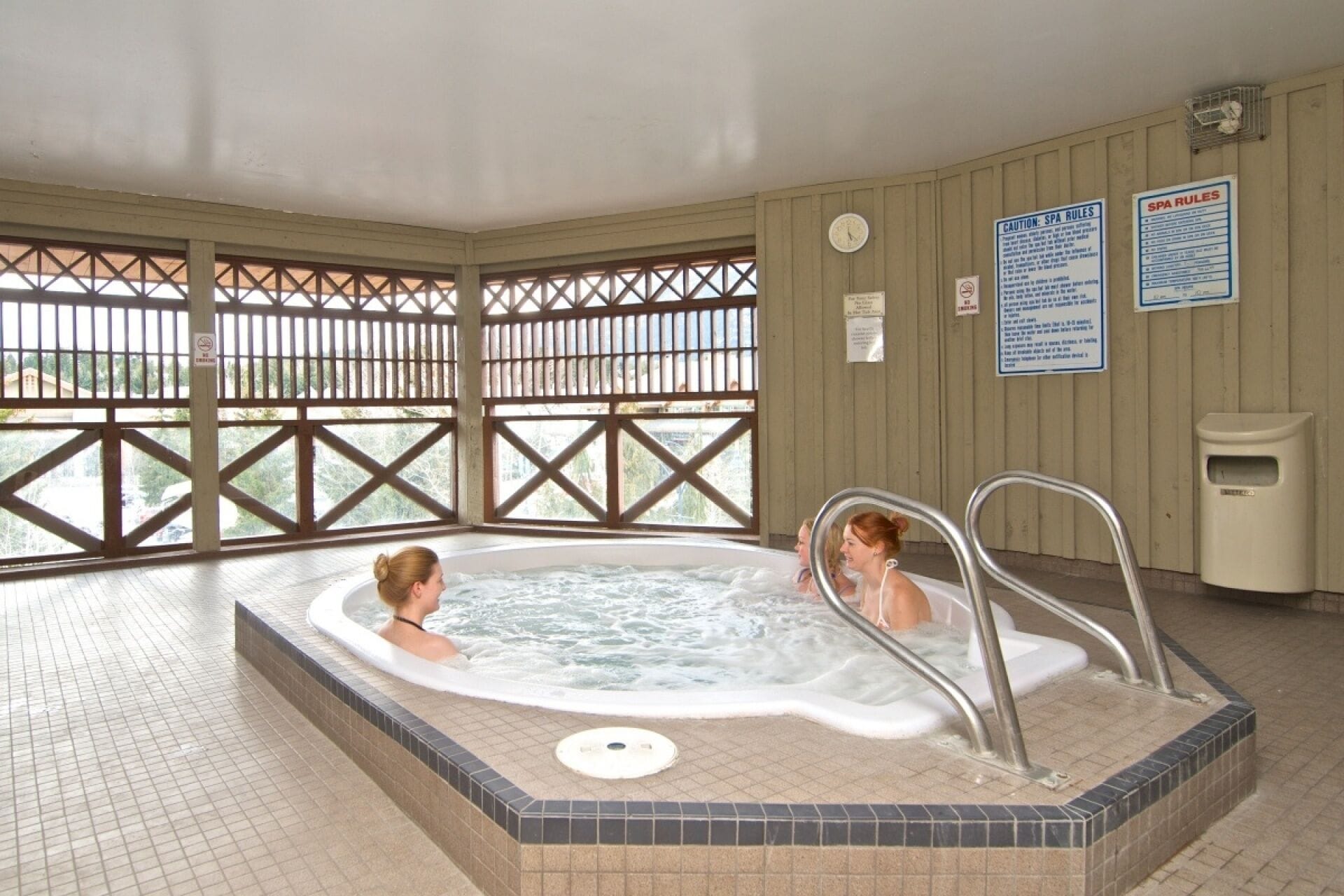 A hot tub area with two people, a clock, and spa rules signs on the wall.