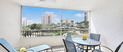 A balcony with a table and chairs, a ceiling fan, and a view of high-rise buildings.