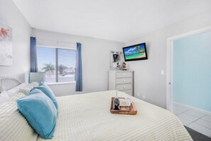 A bedroom with a bed, a dresser, a TV, and a window with curtains.