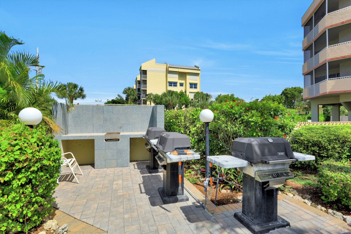 Un espace extérieur aménagé en terrasse, avec deux barbecues, un coin salon et une vue sur un bâtiment jaune en arrière-plan.