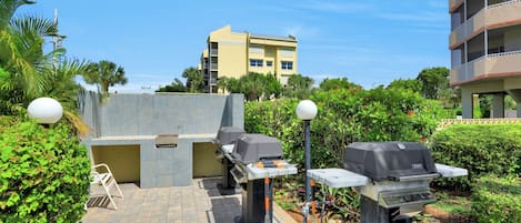 An outdoor patio area with two barbecue grills, a seating area, and a view of a yellow building in the background.